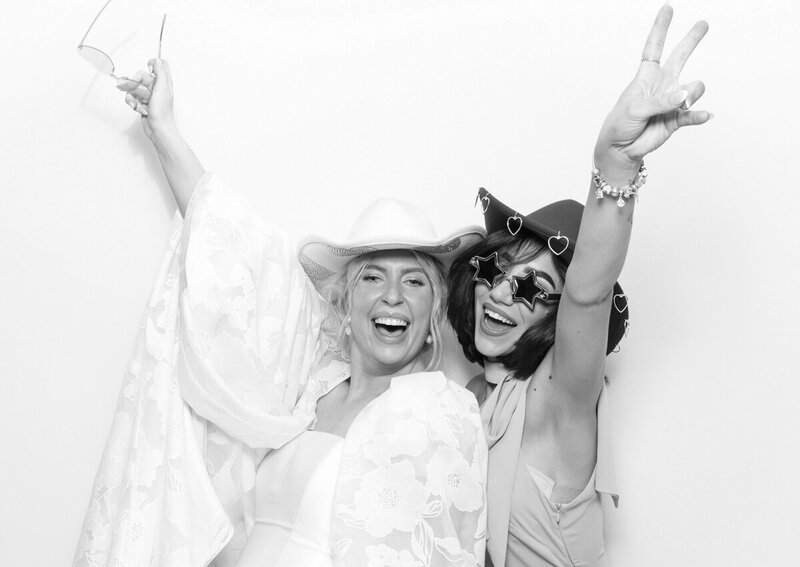 Black and white filter for 2 guests posing against a white backdrop, during a wedding party entertainment, for Mad Hat Photo Booth at Kin House