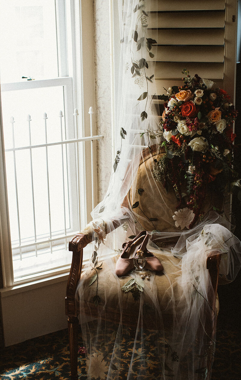 wedding flowers, veil, and shoes on a chair next to a window