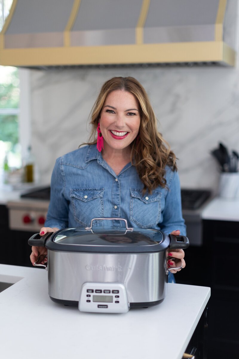 woman with dark hair in jean shirt with pink earrings and crockpot in her kitchen