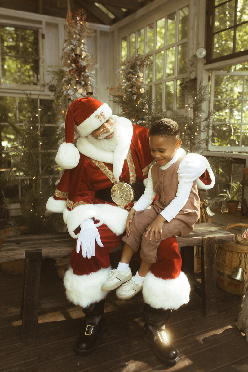A little boy sitting on the lap of The Black Santa of Atlanta telling him all his Christmas wishes. 