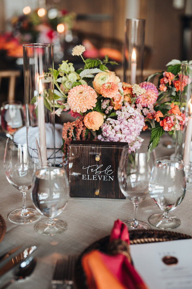 A wedding reception table with water glasses, flowers, and a table number sign with customized calligraphy by Life in Letters.