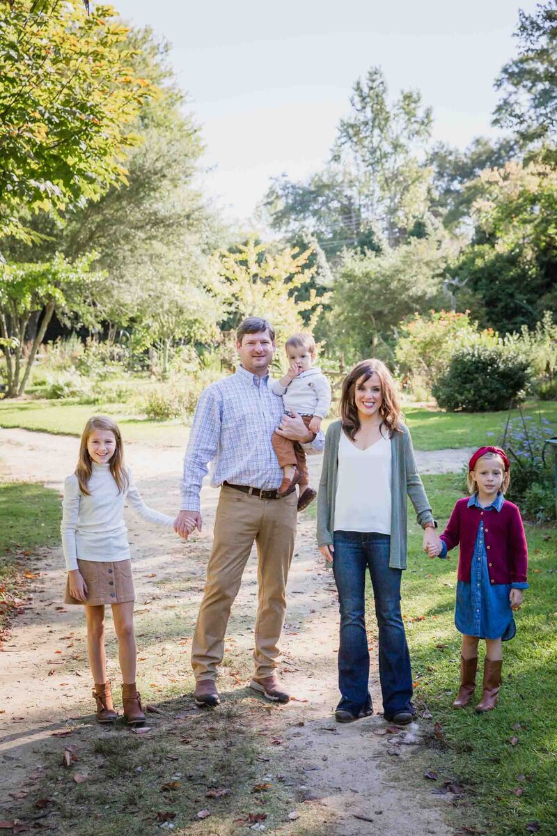 A family walks down a dirt path holding hands toward  the camera during their family portraits with Salina Korn Photography.