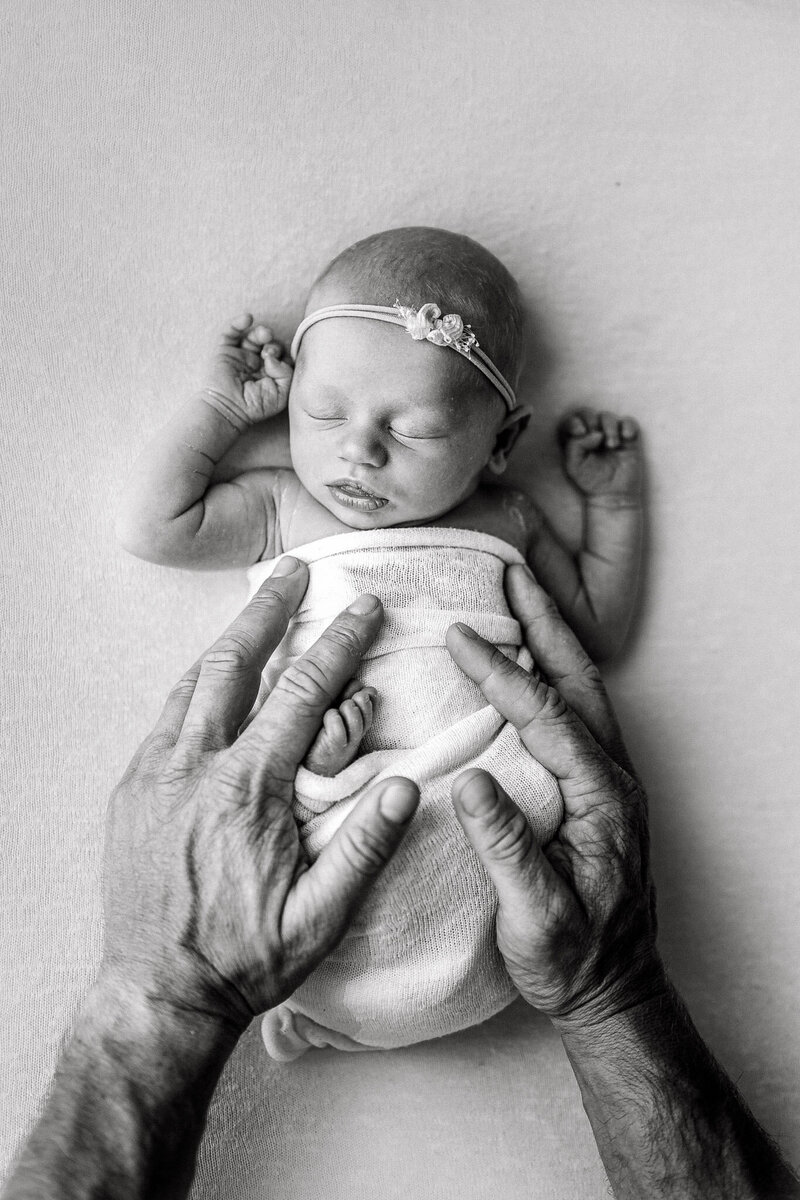 baby girl  wrapped in white  with her dads hands holding her
