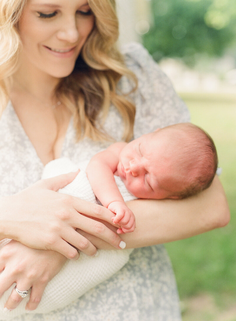 Mom holding newborn baby and smiling at him while he holds her finger during their newborn photography session in Raleigh NC. Photographed by Raleigh Newborn photographers A.J. Dunlap Photography.