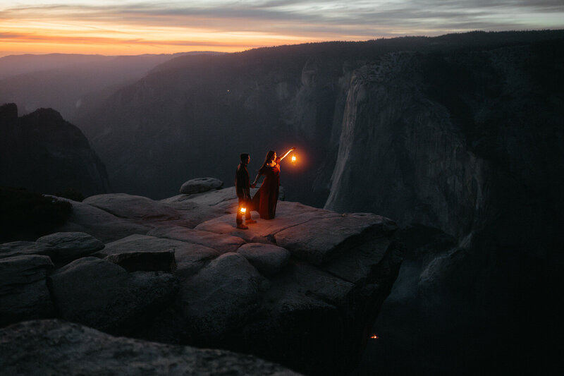 Couple stands on the edge of a cliff with lanterns at Taft Point, the best Yosemite Elopement Location