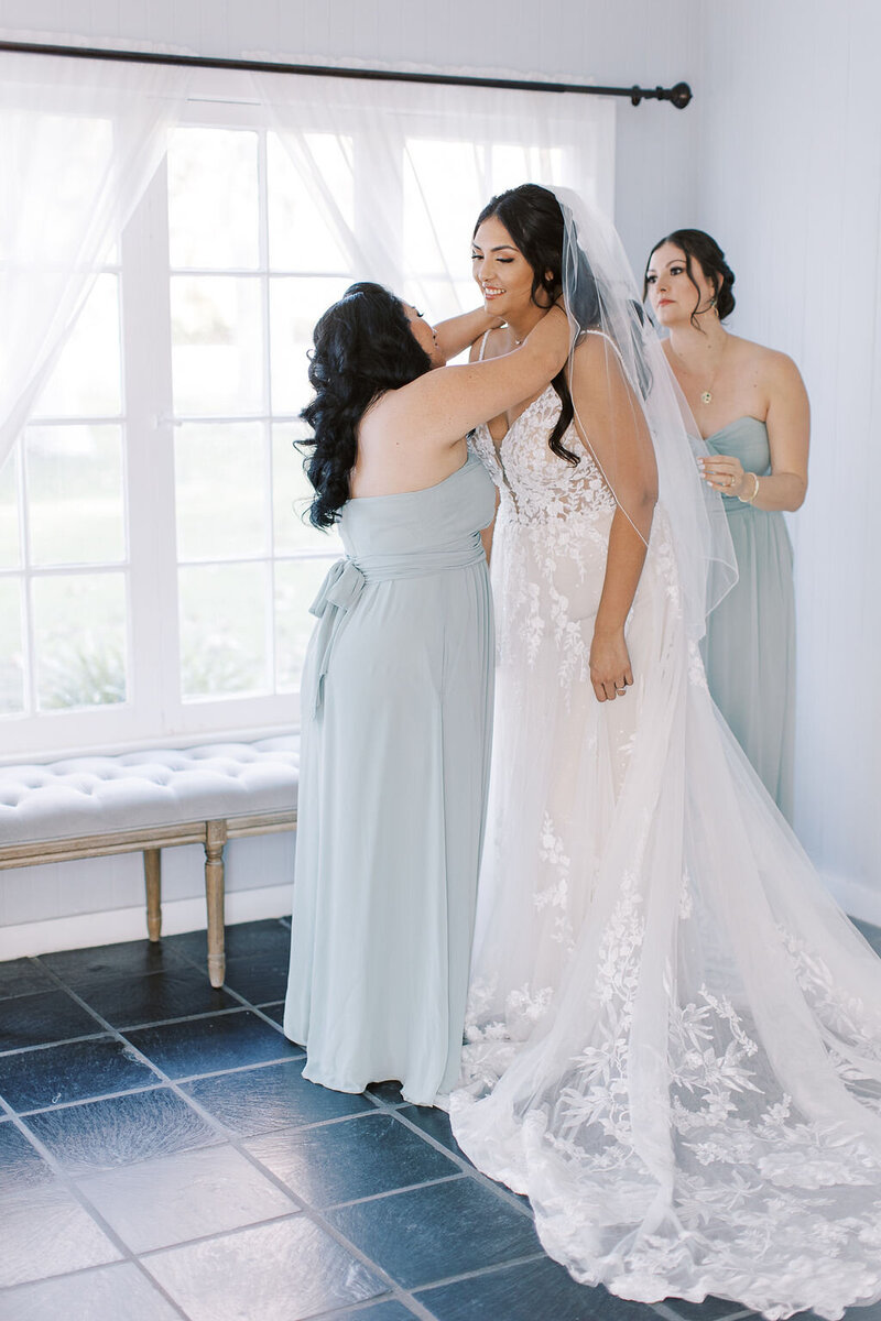 3-radiant-love-events-2-bridesmaids-helping-bride-get-ready-by-window-blue-floors-romantic-elegant-timeless