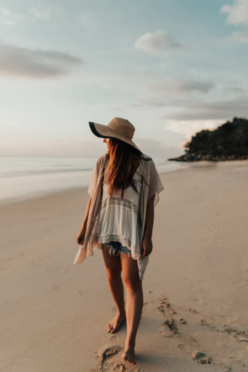 Girl on beach with large beach hat looking at the ocean