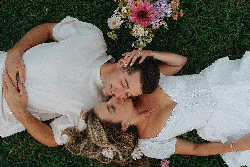 couple lying on grass with flowers during engagement photos, captured by Elsie Goodman, an NYC engagement and couples photographer