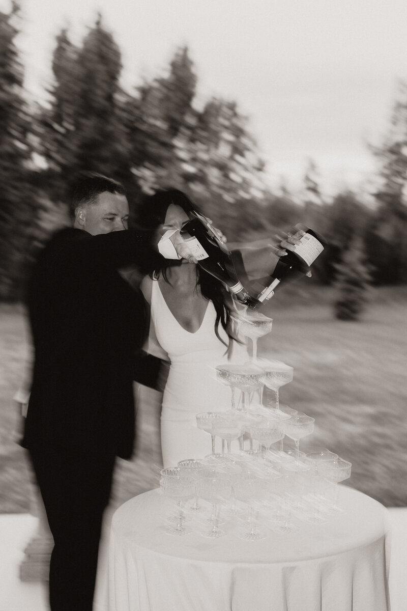 Black and white photo of bride and groom pouring champagne onto a champagne tower.