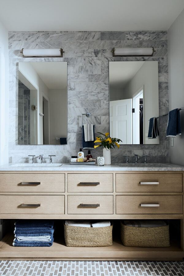 A modern primary bathroom in a historic Hingham home by the best Boston interior designers, featuring an oak vanity, marble backsplash, mosaic flooring, and polished nickel fixtures.