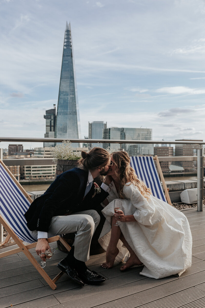 Bride and Groom sit in deck chairs and kiss with The Shard in the background