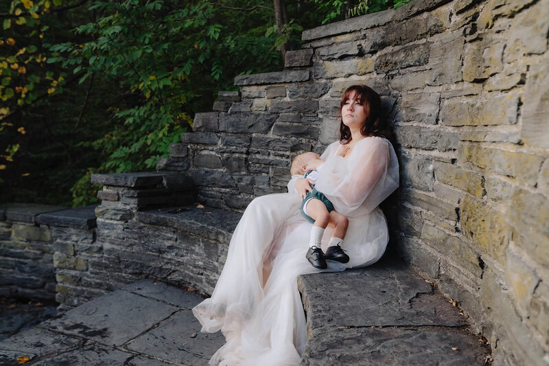 Bride breastfeeding young child sitting on stone bench