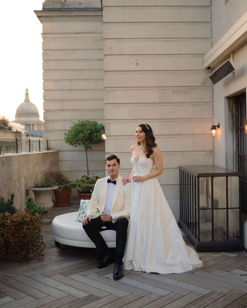 a sophisticated wedding couple pose on the rooftop of luxury wedding venue the ned london with st pauls cathedral in the background