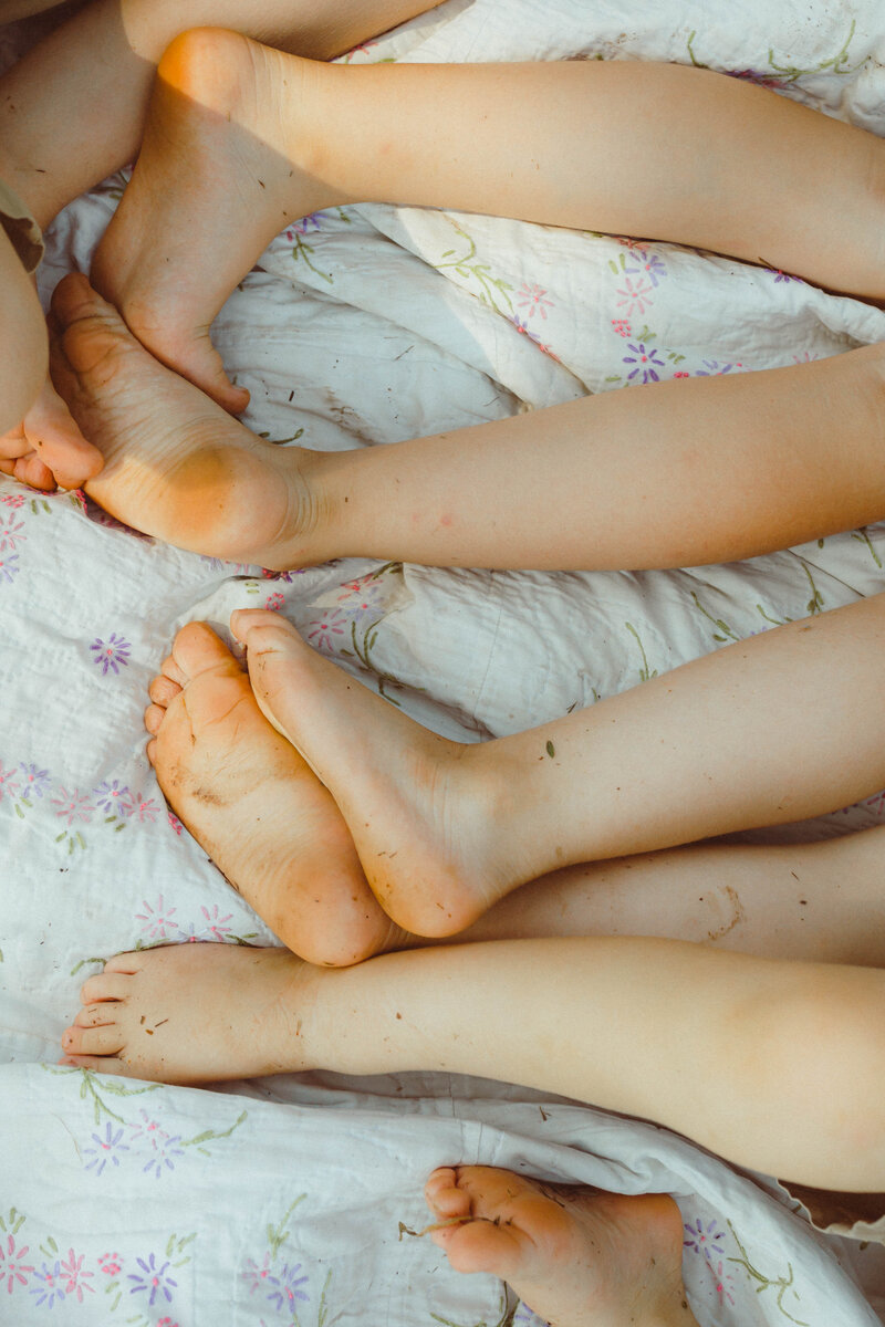 Close-up of children's feet covered in grass, lying on a blanket, captured in a documentary-style photo in Columbia, MO.