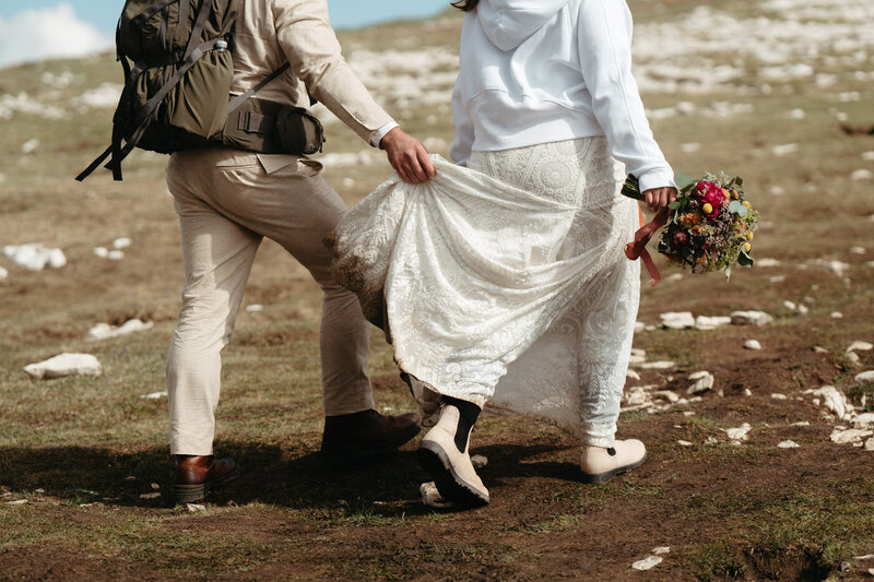 up close photo: Groom holds brides dress as she hikes and holds her Dolomites florist bouquet during their dolomites elopement