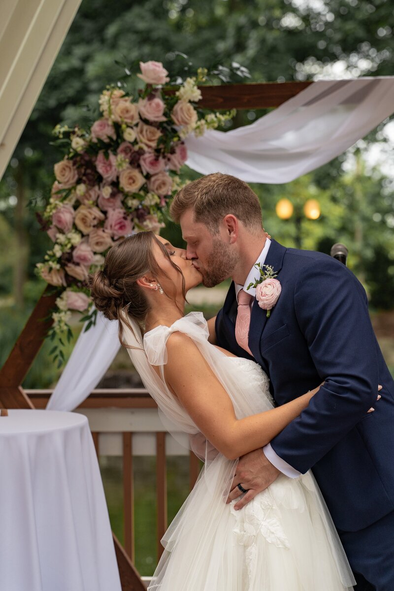 Groom dips the bride into a kiss under a floral arch at a Lizton Lodge wedding in Lizton, Indiana