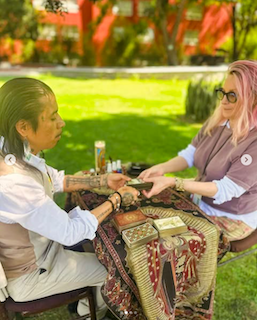 A practitioner offers a tarot and intuitive hand-reading session to an attendee in a peaceful outdoor garden setting during the San Miguel Writers Conference wellness program.