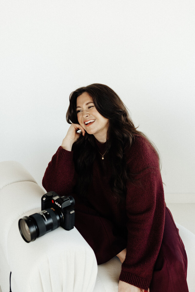 Headshot of Elisabeth Eden holding glasses, holding a coffee mug, and leaning forward while laughing at the camera, capturing a warm and approachable personal brand moment.