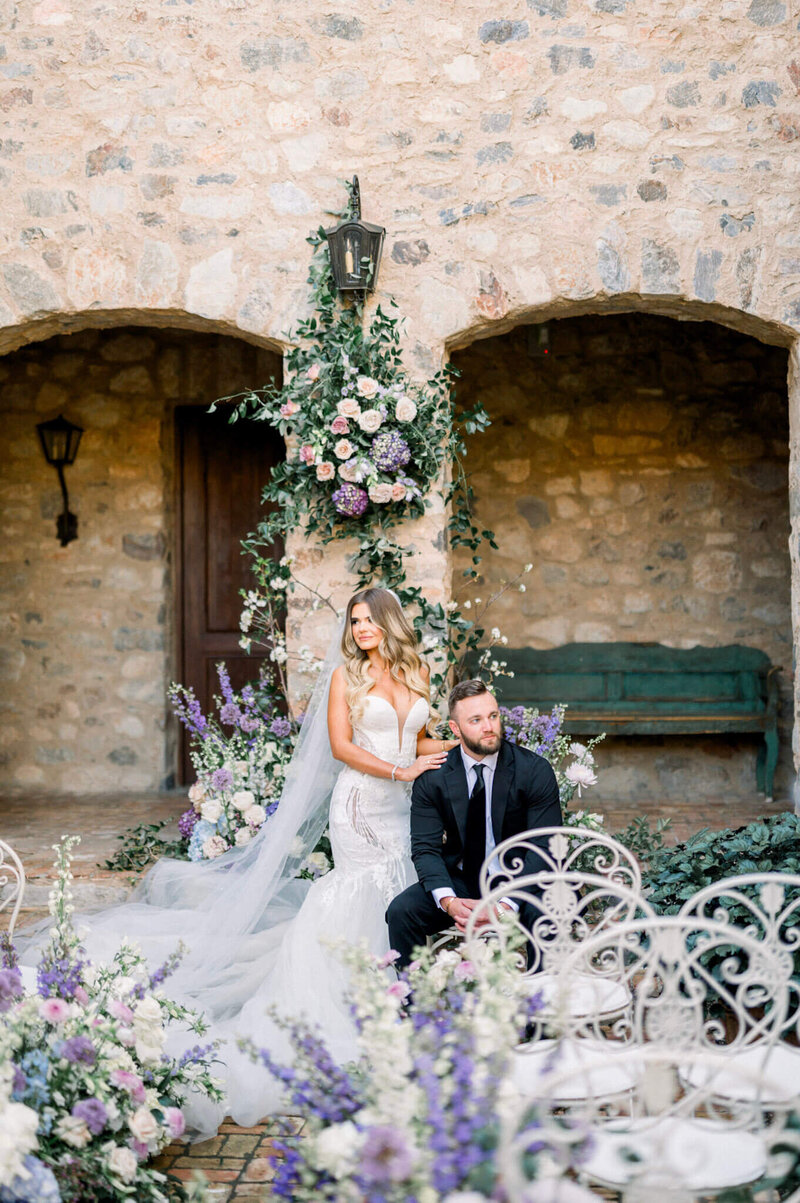 Newlyweds posing by stone wall with lush floral installation - Scottsdale wedding photographer.