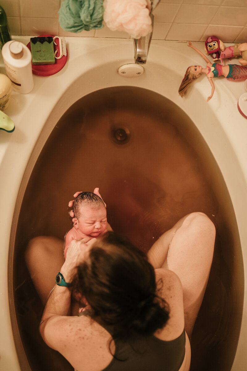 Mother delivering her baby in a birth pool surrounded by calm support — home birth photography in Weatherford by Poppy + Blue Photography