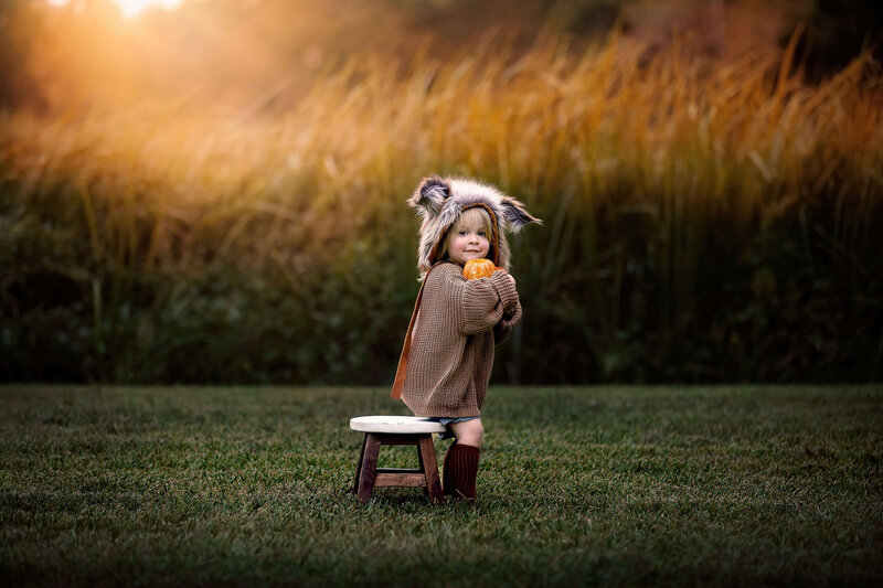Adorable little girl wearing a fox bonnet holding a pumpkin