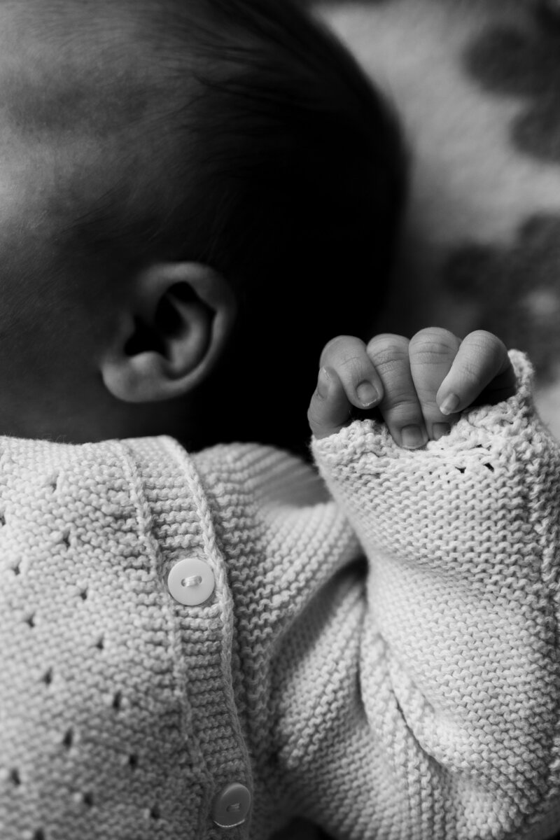 Een schattige baby ligt op een zachte deken, gekleed in een gebreid truitje, met een vredige uitstraling.