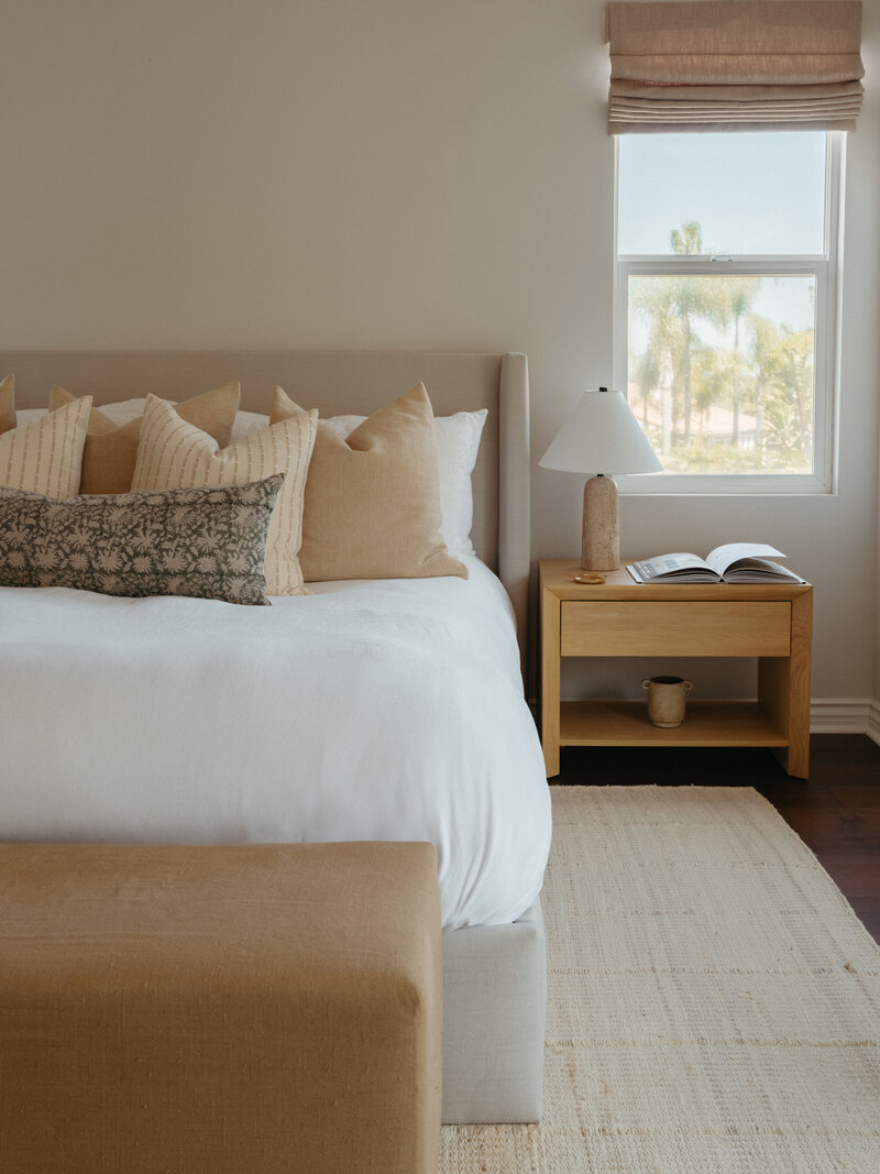 Bedroom study corner with fluffy cream chair, rust pillow, gold lamp, and foot cushion in Encinitas, California.