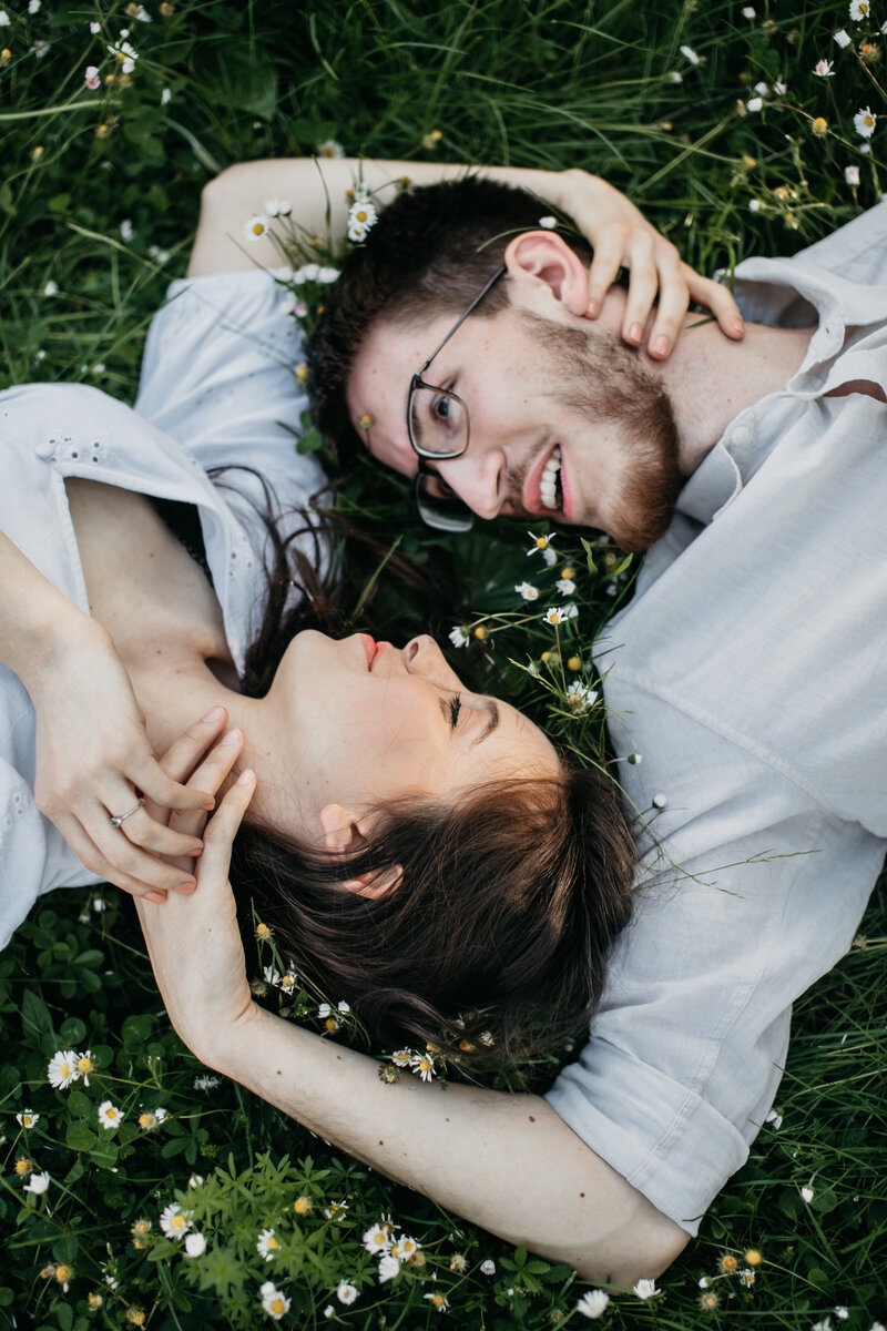 Couple lying on their backs on the grass, head to head, captured from above in a peaceful and intimate moment in Germany.