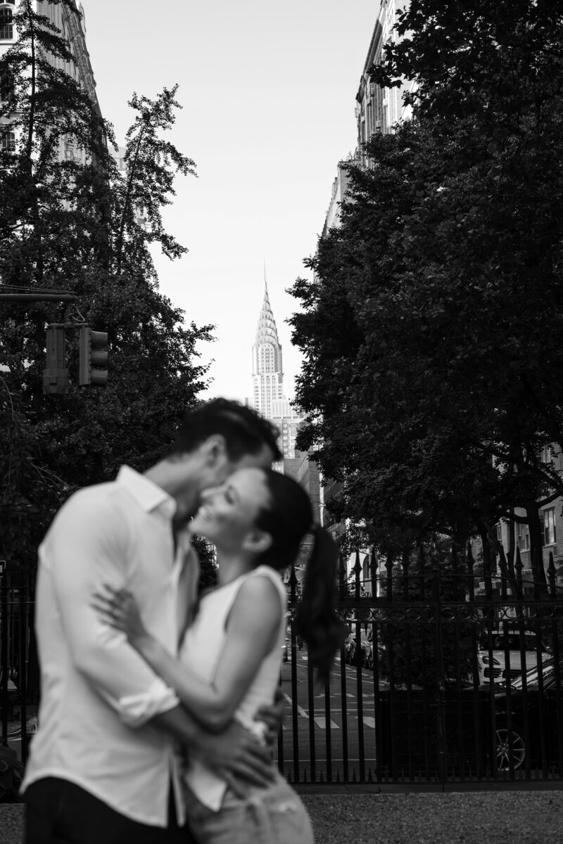Couple in Gramercy Park enjoying an embrace during their proposal with the Chrysler building in the background.