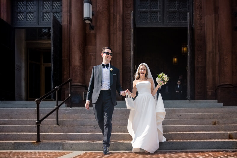 A man and woman hold hands walking down the steps of a courthouse