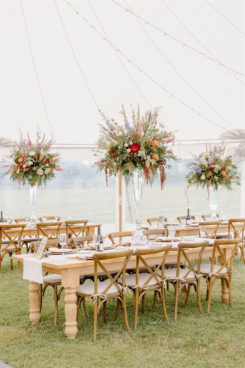 Ornate farm tables under a pole tent wedding table scapes with incredible lush floral trumpet floral arrangement photo courtesy of Jenna Brisson Photography