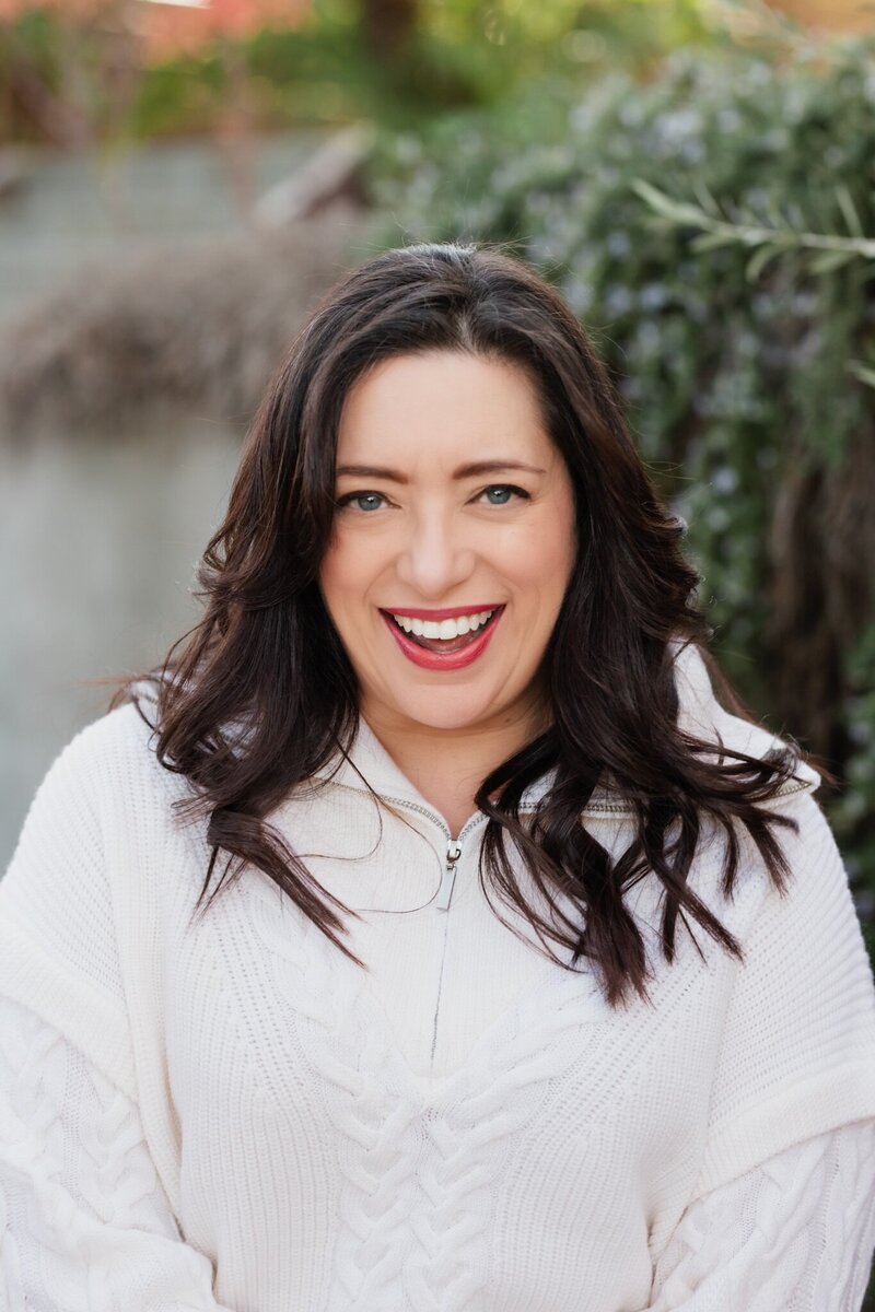 Renee Dalo smiles in blue sweater with red trip with bright red lipstick on