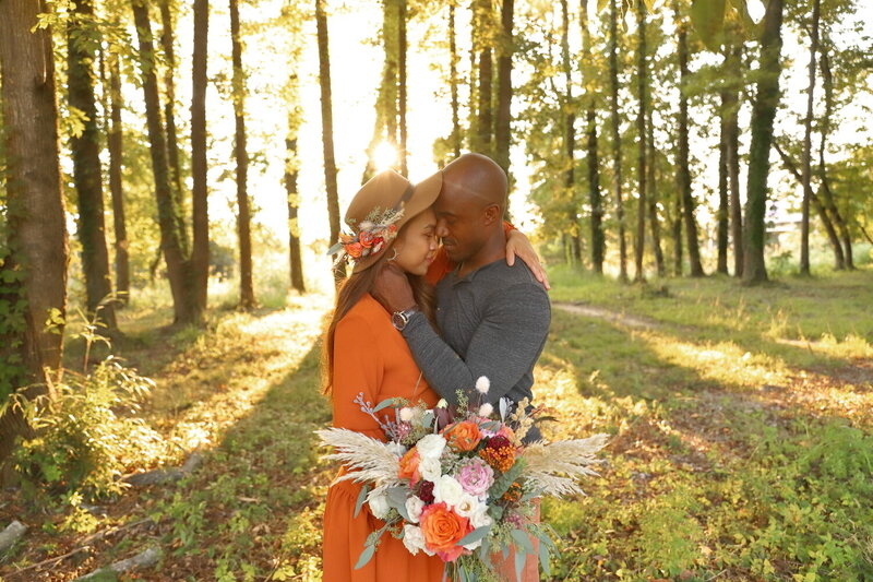 Interracial couple embracing during golden hour  anniversary session in the woods with boho bouquet
