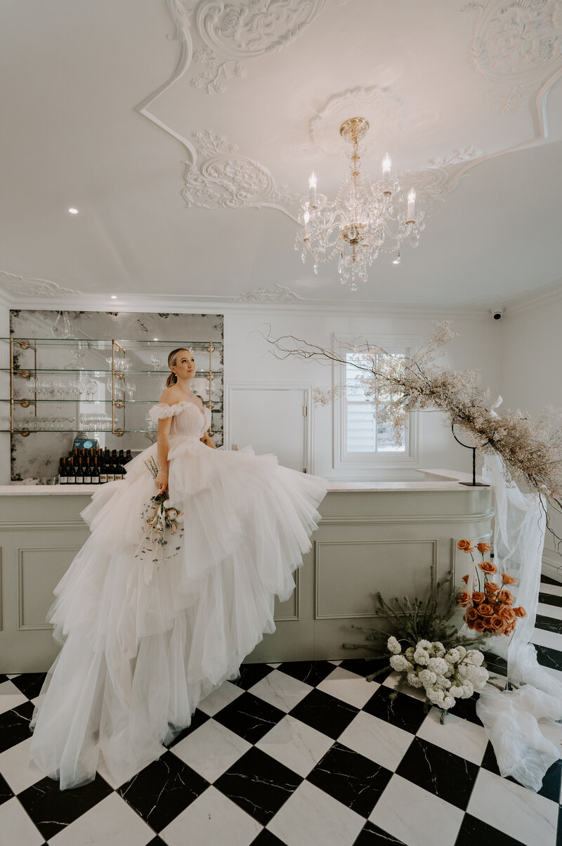 bride seated on the bar at Kwila Lodge, low ponytail, peach makeup, spectacular dress