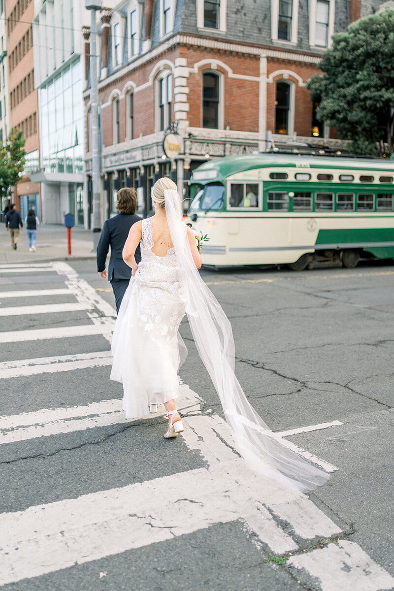 A bride in a beautiful gown with a long veil crosses a San Francisco street, capturing the essence of urban elegance.