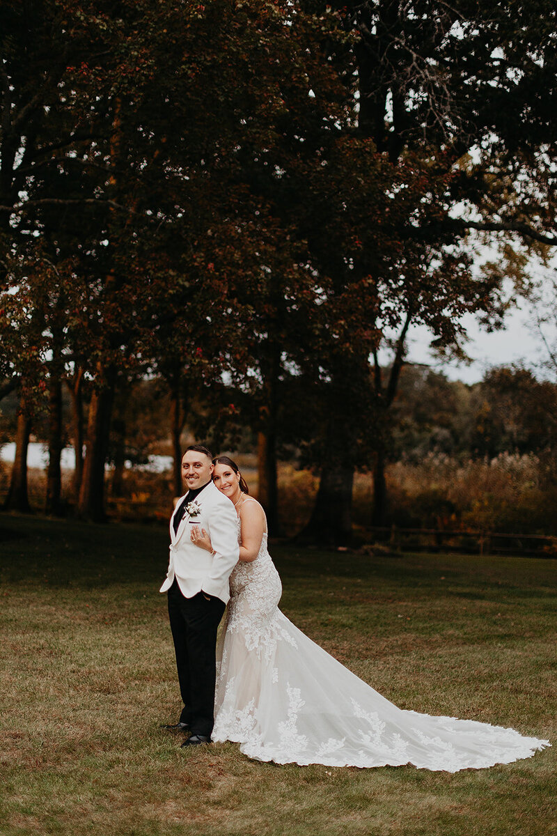 In the midst of a beautiful lawn, the bride embraces the groom from behind, playfully engaged in a moment of disagreement, yet their smiles convey a shared joy.