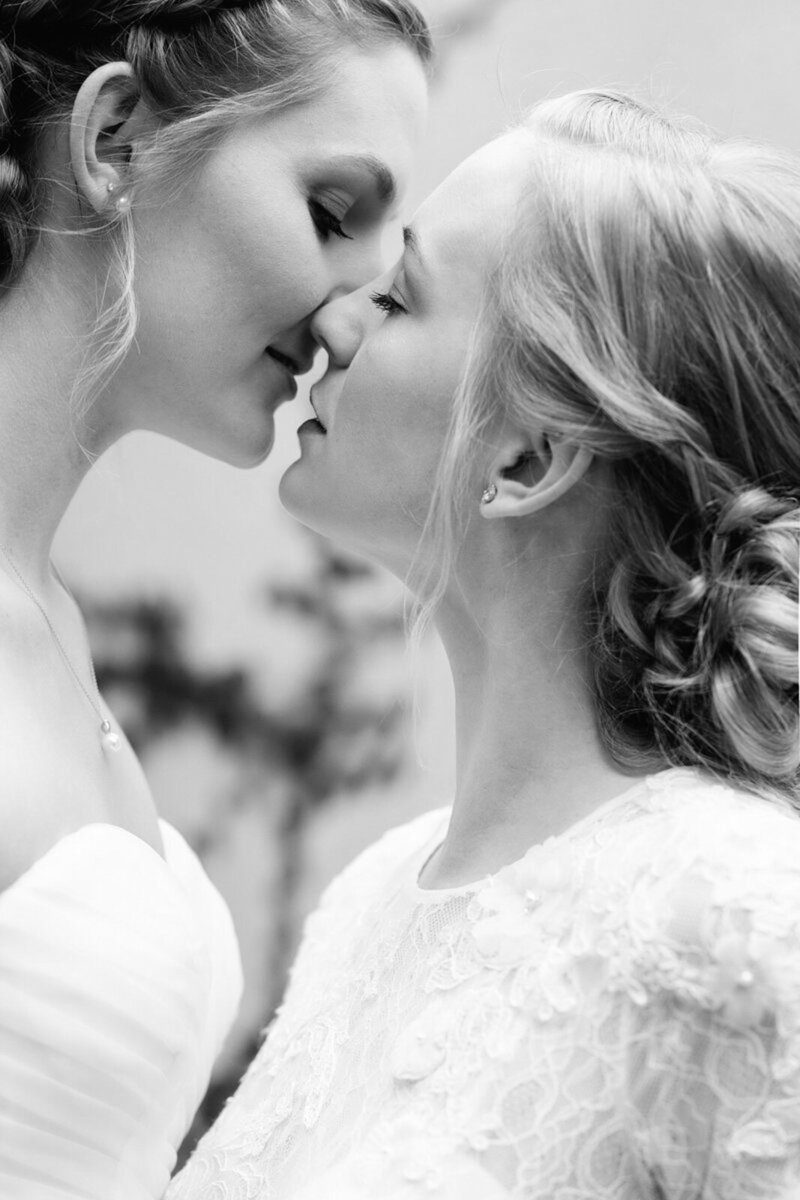 Close-up portrait of two brides at their same-sex wedding, leaning in for an intimate kiss.
