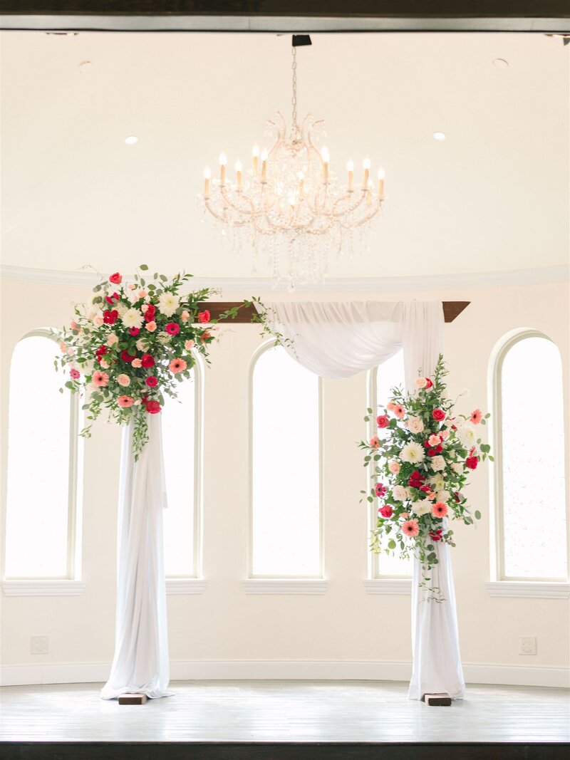 ceremony arch with bright flowers in shades of hot pink, light pink and pale pink and white draping