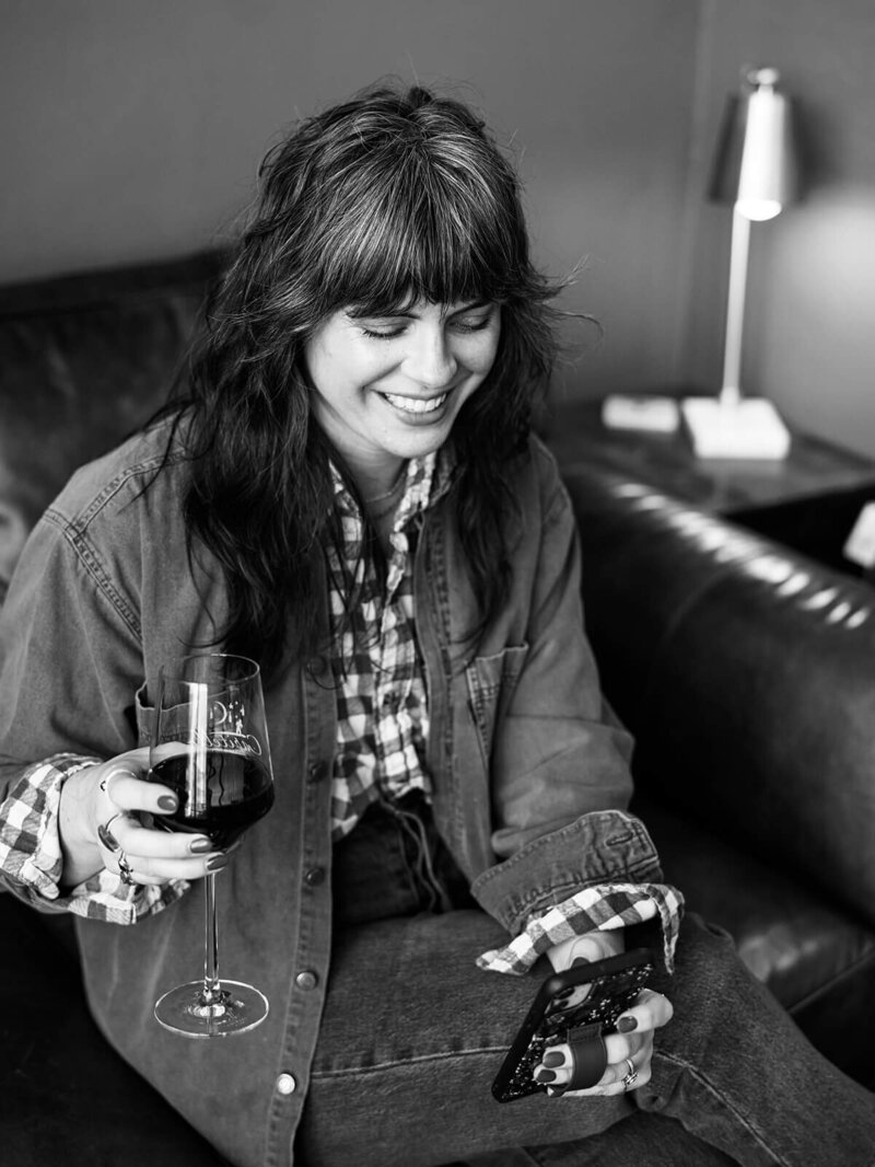 Bloem Creations founder Carrie holds a glass of wine and smiles while looking at her phone.