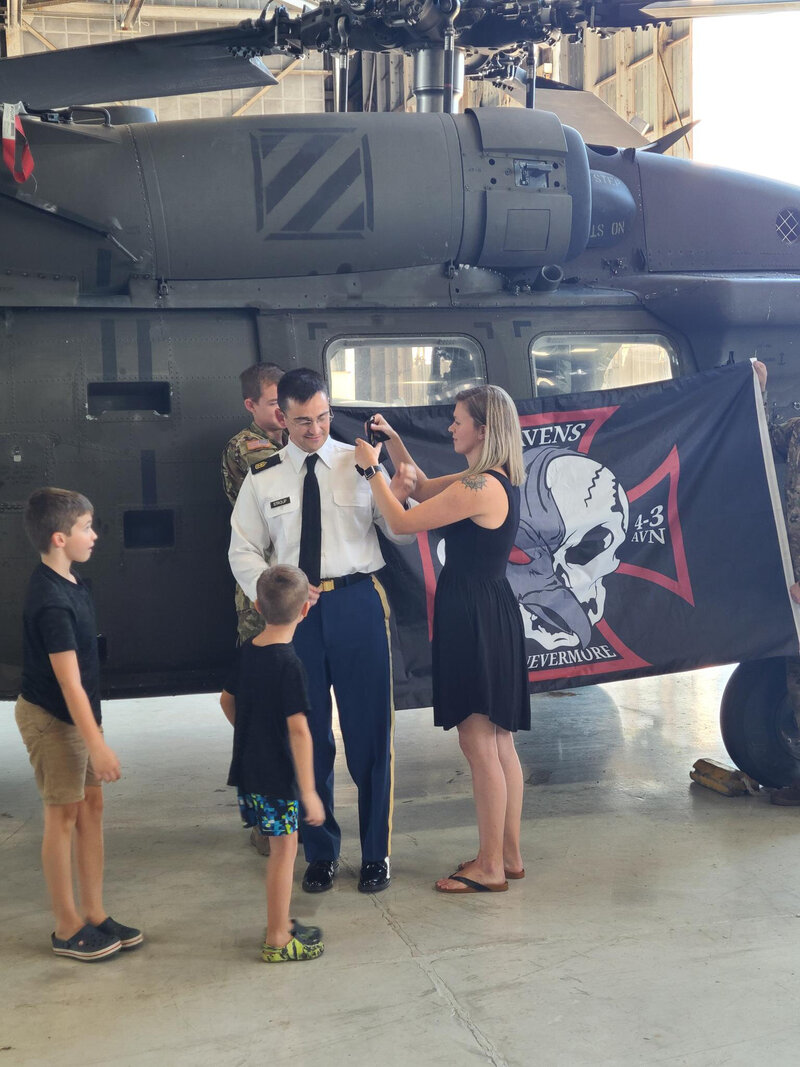Tammy changing her husband's rank at promotion ceremony with their children in front of helicopter