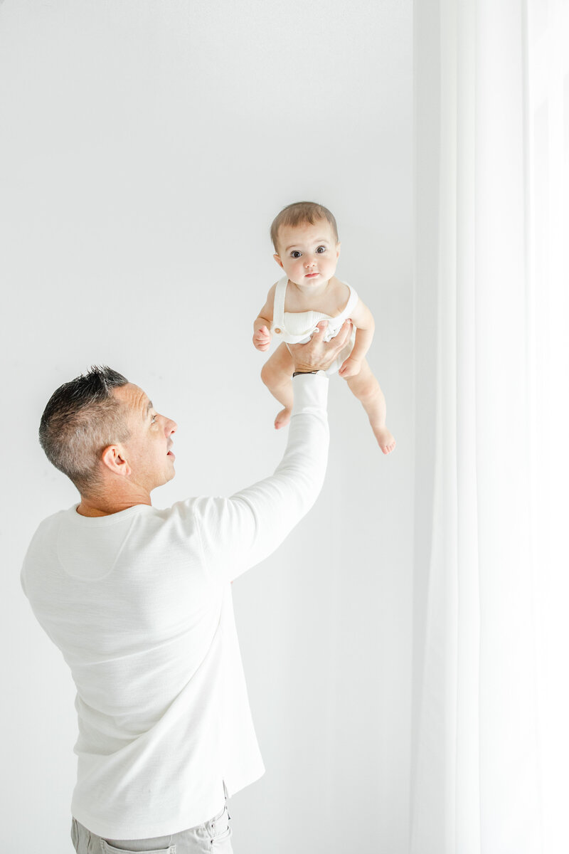 Dad holds 6 month old baby in the air during an in-studio baby portrait session