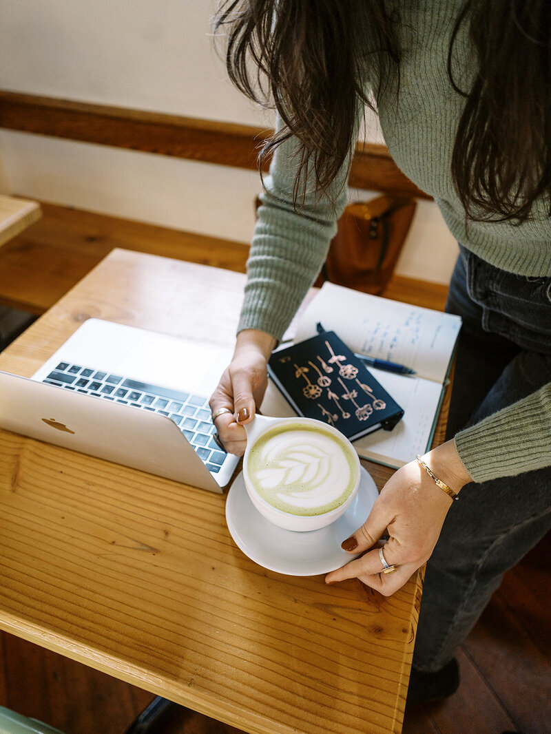 A faceless woman setting down a matcha latte next to a laptop. 