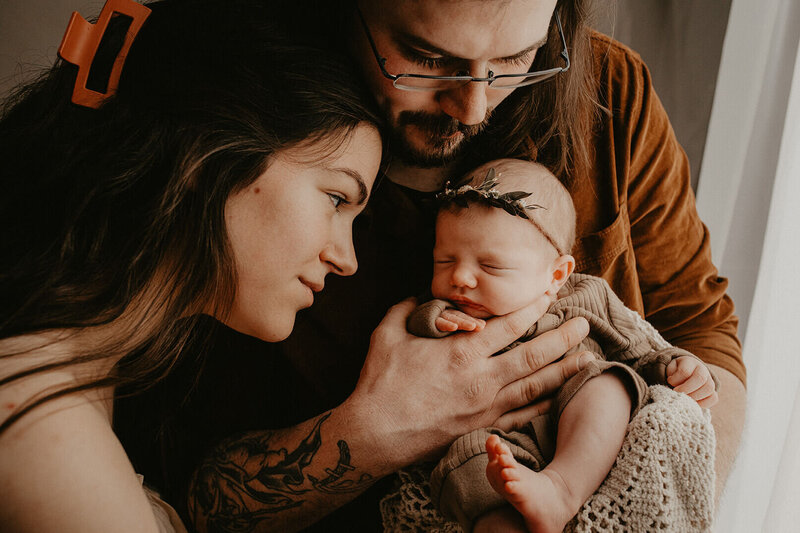a dad holding his newborn baby girl against his chest while the mom lookings adoringly at their new baby