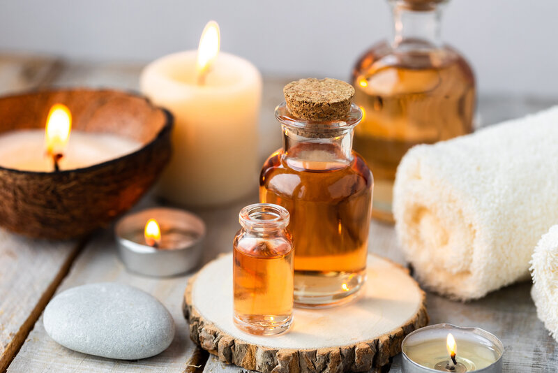 Close-up of spa essentials including bottles of massage oil, rolled towel, candles, and smooth stones on a wooden surface.