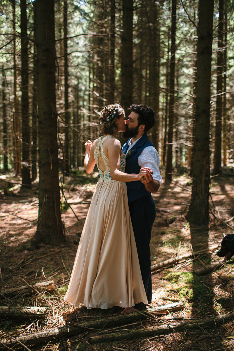 Wedding in the woods - a couple embrace in the woods on their wedding day, the bride wearing a home made dress in champagne with blue embroidery 