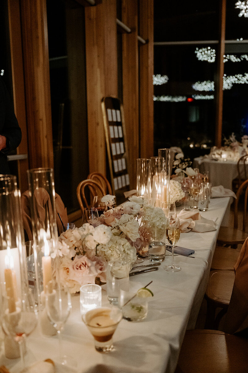 Close-up of reception table with white hydrangea, neutral roses, and bleached fern in lucite vases, styled with candlelight at Jenay and Daniel’s wedding by Summer Robbins Flowers in Central Oregon