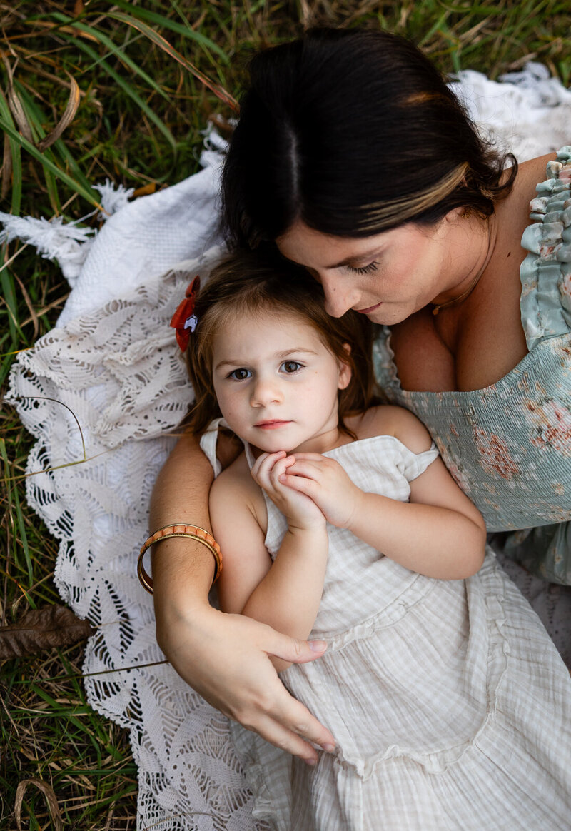 Mother holding her daughter while they lay on a blanket in a field in the park in Bonne Terre, Missouri. 