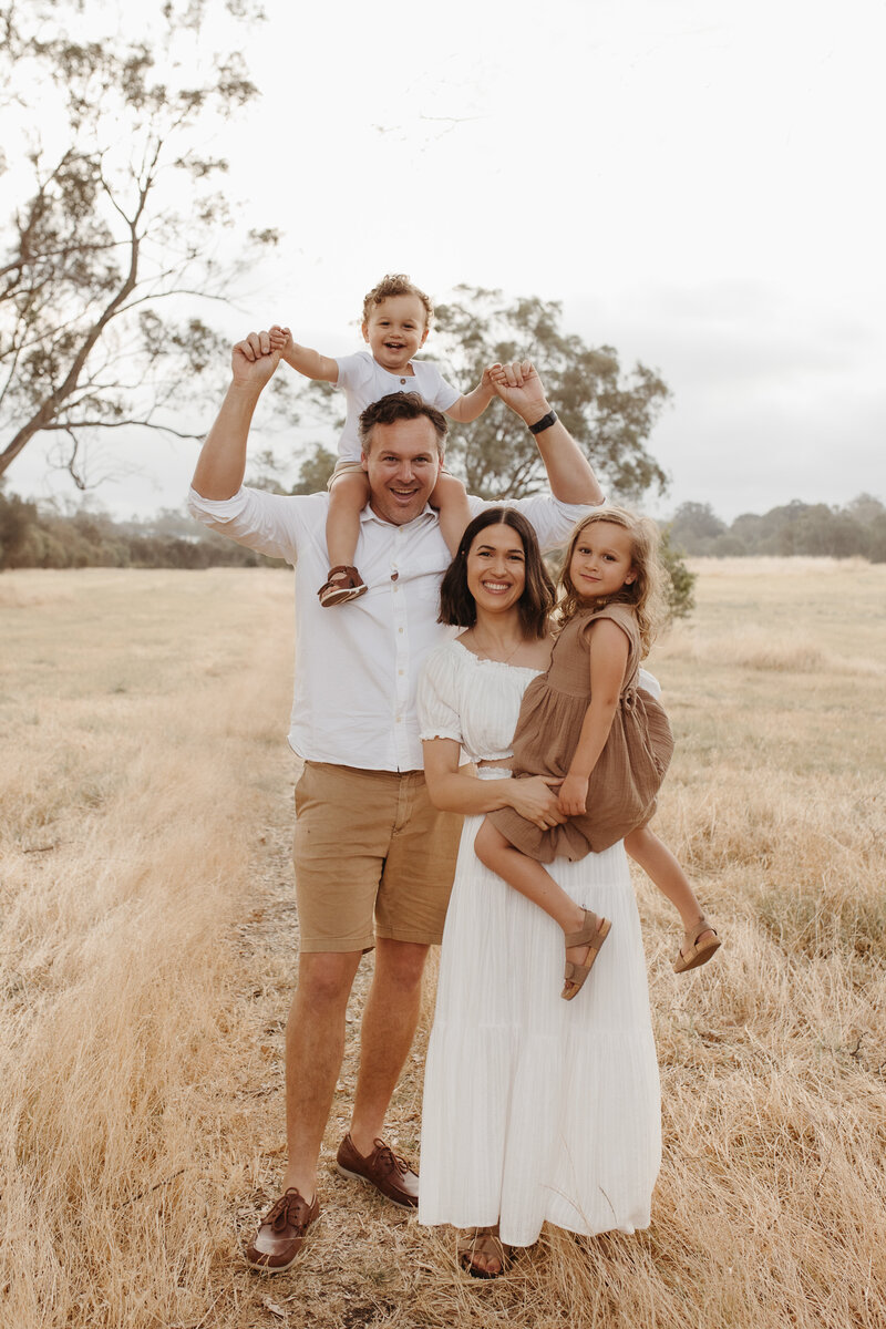 Family session in Perth. Relaxed family stands together and smiles in a field.