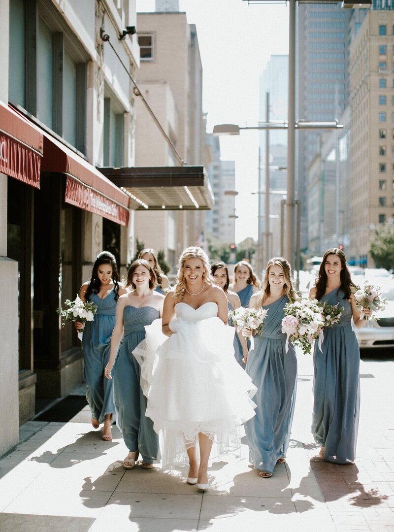 bride and bridesmaids walk down the sidewalk of a busy city