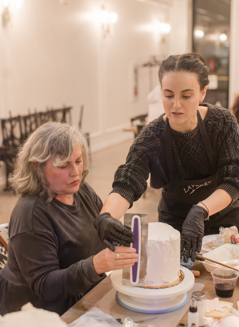 Layered Cake Artistry owner Conetta teaching a student how to frost a cake.